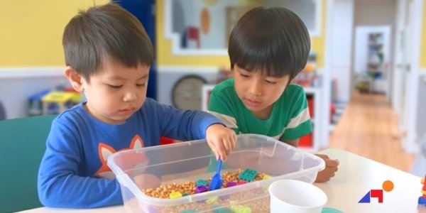 Two preschool boys engaged in sensory play with colored beads at KidStart Therapy Integrated Learning Program, demonstrating therapy routines that build skill generalization for daycare success.